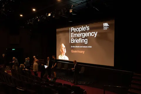 The film's title slide, People's Emergency Briefing Guernsey, on the cinema screen in a darkened auditorium