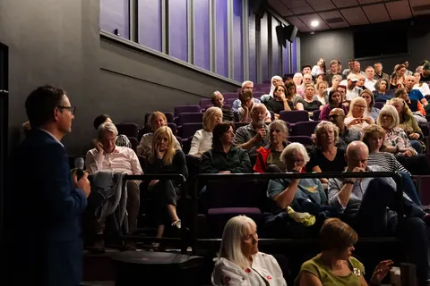 A person holding a microphone beside the seated audience