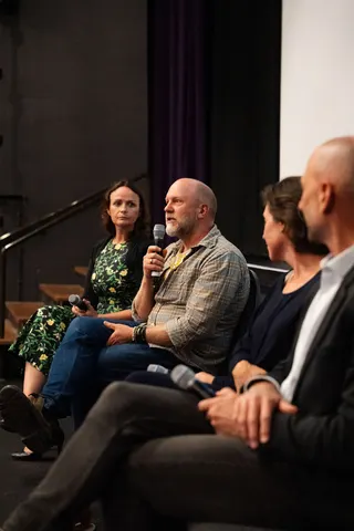 A seated panel, with a bearded panellist speaking into a microphone