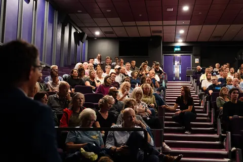 Tiered rows of seated people filling the auditorium, seen from the side