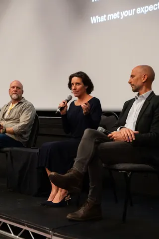 A woman seated among the panel speaking into a microphone