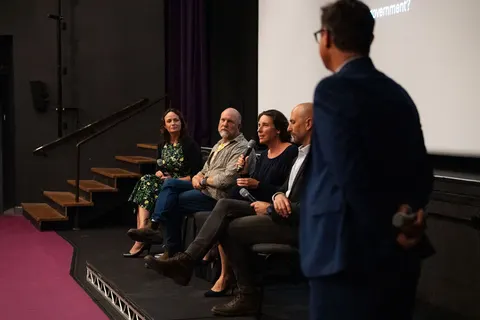 A standing facilitator facing the seated panel on stage