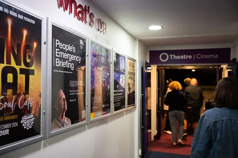 Posters along the foyer wall, with people entering the Theatre and Cinema doorway
