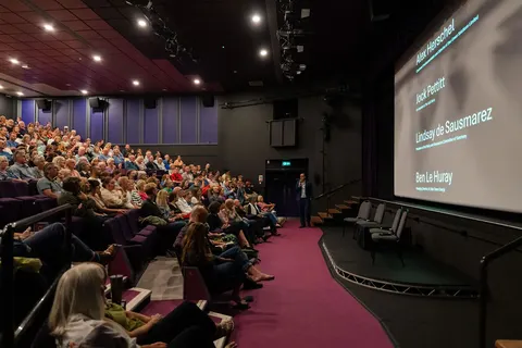 A wide view of the auditorium audience facing the screen and stage