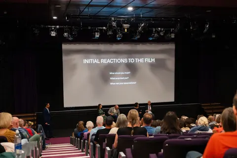 Audience members in tiered seating facing a screen headed Initial reactions to the film